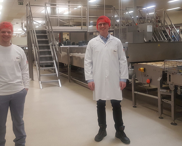 Een man in witte jas en rode hoofdband die in een fabriek staat