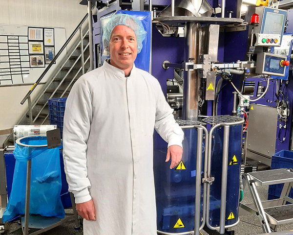 Een man in een witte mantel en haarnet die voor een machine staat